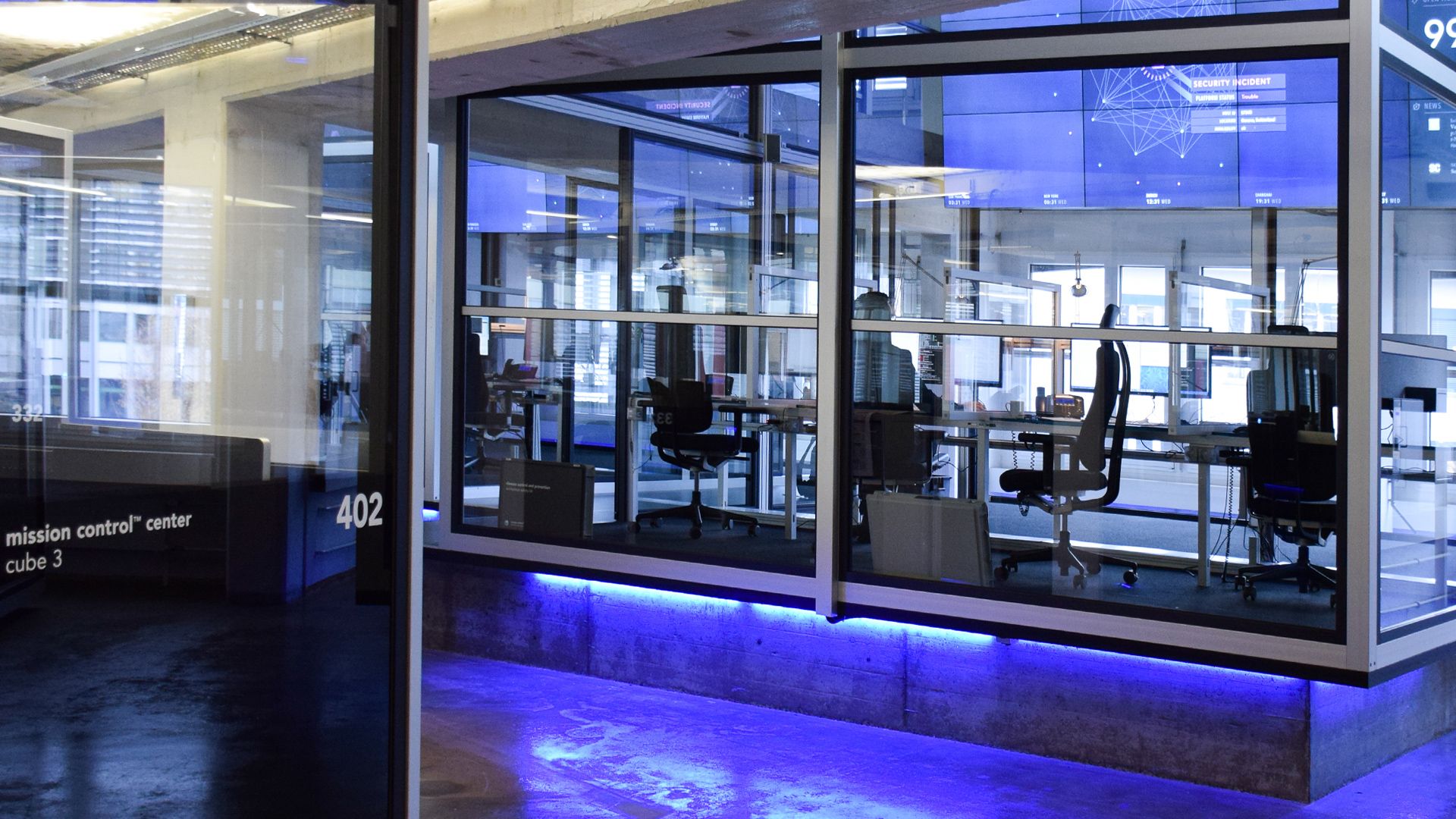 Open Systems Mission Control center at night, the wall display glowing behind glass with blue LED lighting