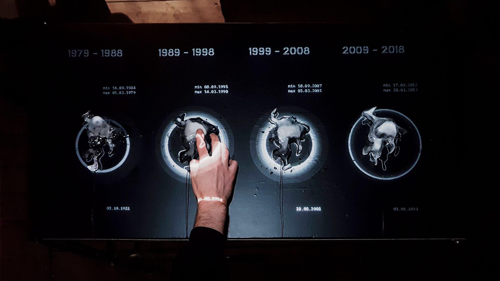 2455700km2 installation: four melting Arctic-shaped ice blocks labeled by decade from 1979 to 2018, a hand touching one