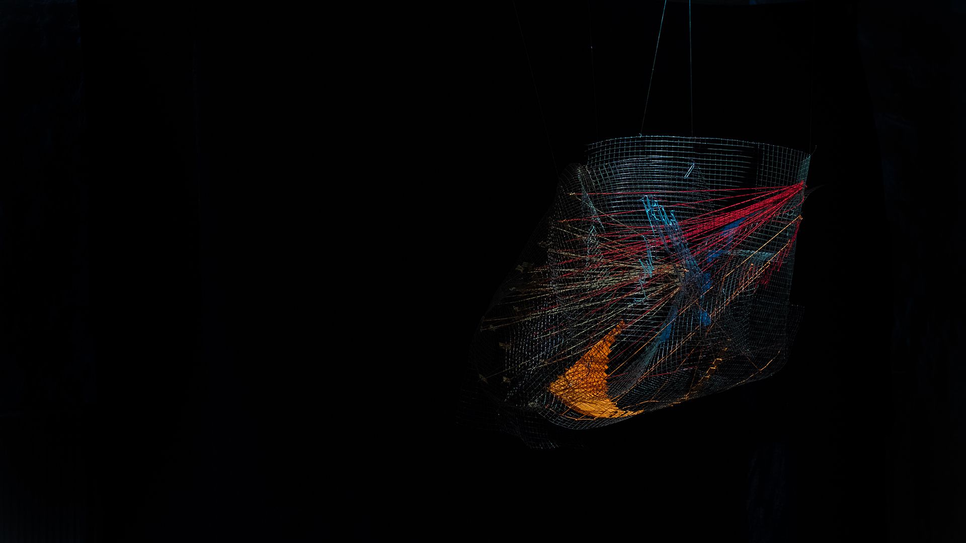 High Dimensional Data Narrative data sculpture, a wire-net form threaded with red, orange and blue lines in darkness