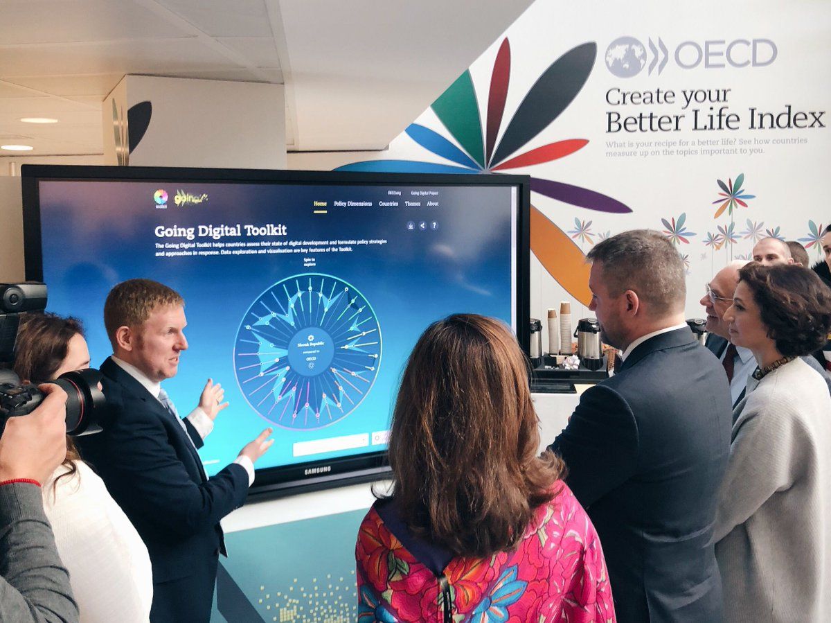 People at an OECD event in front of a Create Your Better Life Index flower mural and interactive screen